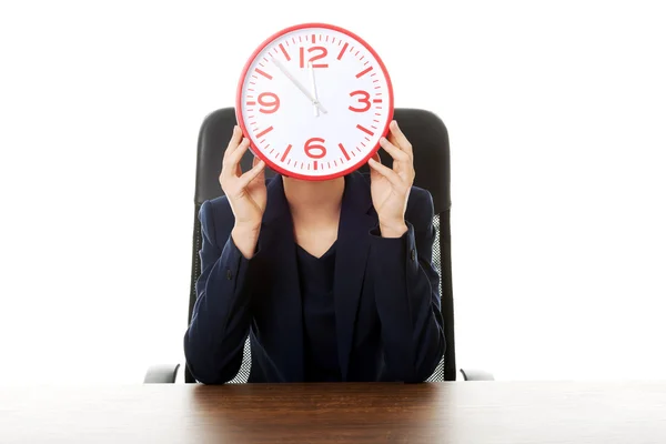 Kobieta siedzi z dużym zegarem w urzędzie — Zdjęcie stockowe