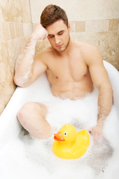 Knappe man nemen van een bad met eend speelgoed. — Stockfoto