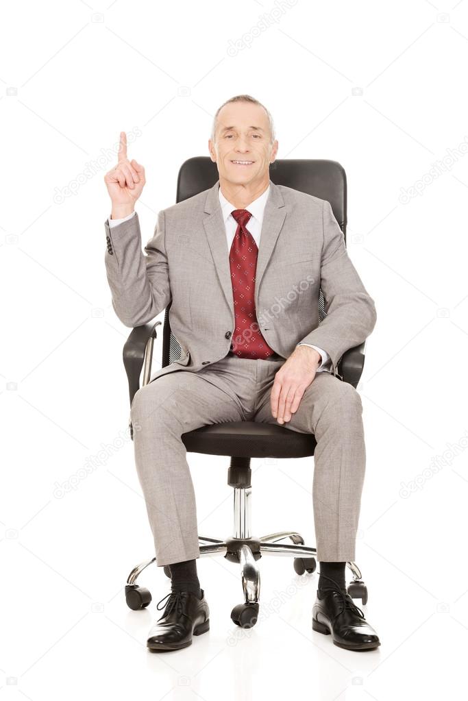 Businessman sitting on armchair and pointing up