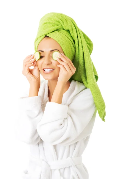 Woman in bathrobe applying cucumber on eyes — Stock Photo, Image