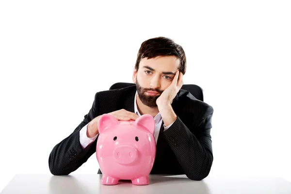 Businessman with piggybank by a desk. Stock Picture
