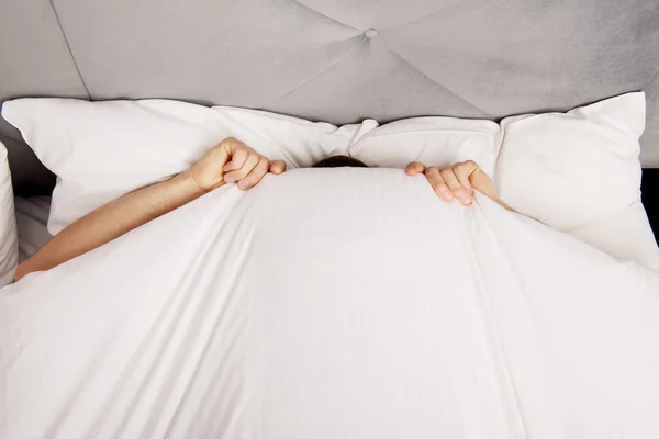 Homem escondido na cama debaixo dos lençóis . — Fotografia de Stock