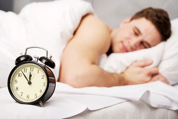 Mann mit Wecker im Schlafzimmer. Stockbild