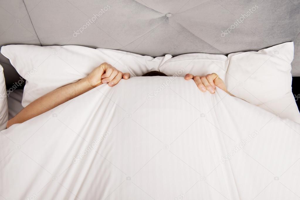 Man hiding in bed under sheets.