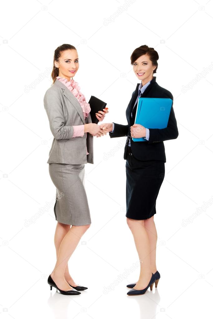 Two women with notebooks giving handshake.