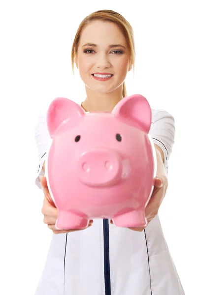 Fiatal női orvos egy piggybank gazdaság. — Stock Fotó