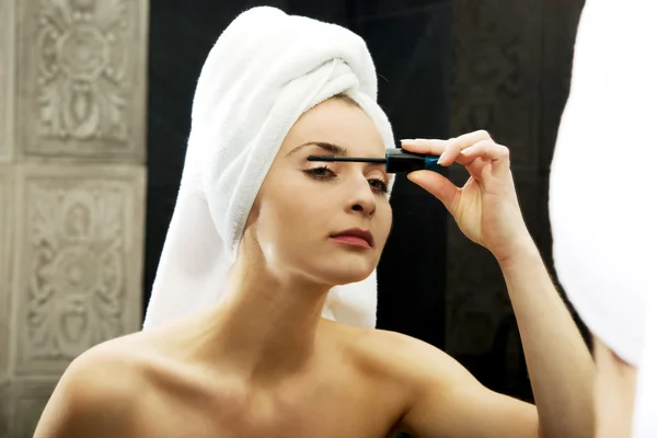 Woman using mascara in bathroom mirror. — Stock Photo, Image