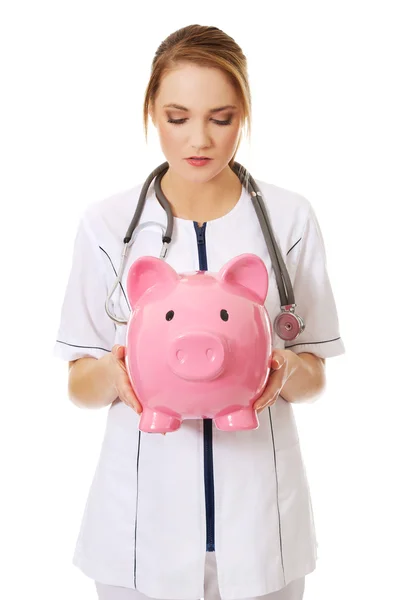 Young female doctor holding a piggybank. — Stock Photo, Image