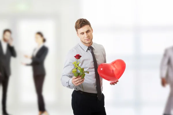 Νεαρός άνδρας με ένα κόκκινο τριαντάφυλλο και μπαλόνι καρδιά. — Φωτογραφία Αρχείου