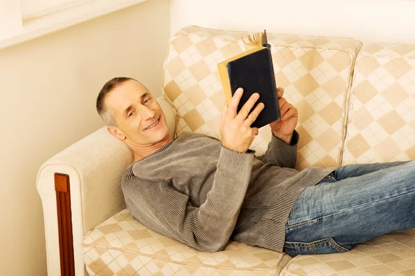 Ontspannen volwassen man lezen van een boek in woonkamer — ストック写真