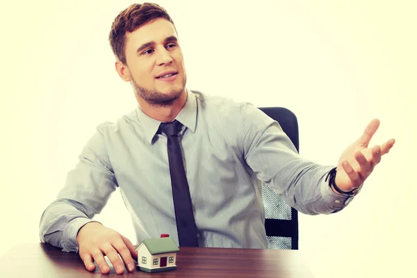 Talking businessman with house model by a desk. — Stock Photo, Image