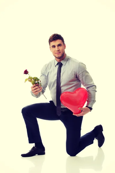 Hombre arrodillado con rosa roja y globo del corazón . — Foto de Stock