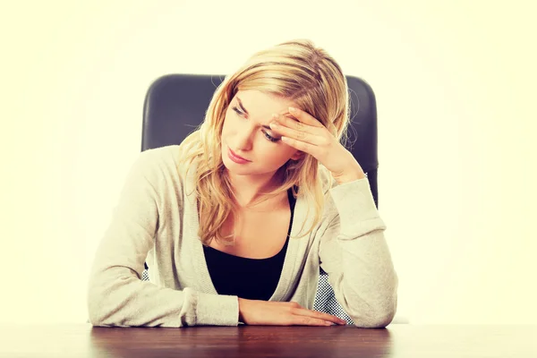 Tired woman sitting at the desk touching head — Stock Photo, Image