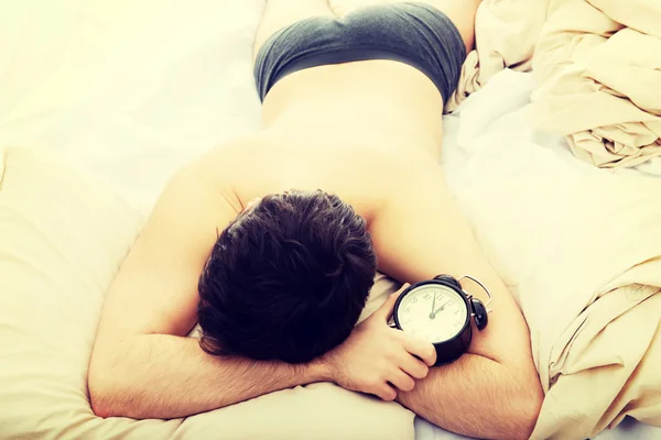 Exhausted man being awakened by an alarm clock. — Stock Photo, Image