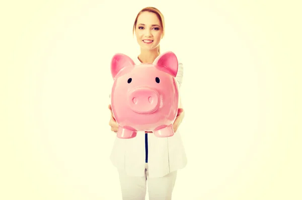 Fiatal női orvos egy piggybank gazdaság. — Stock Fotó