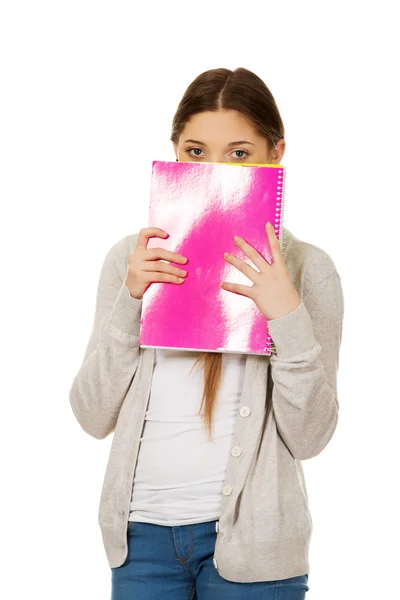Teen woman hiding behind a notebook. — Stock Photo, Image