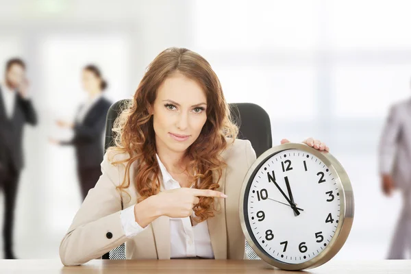 Businesswoman pointing on a clock by a desk. — Stock Photo, Image