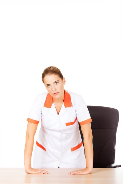 Cansada jovem doutora enfermeira em pé atrás da mesa — Fotografia de Stock