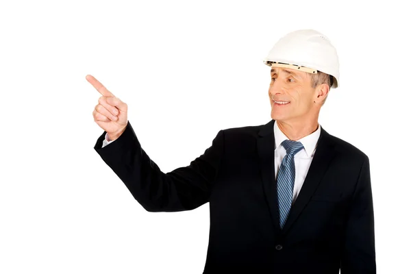 Hombre de negocios sonriente con el sombrero duro apuntando hacia arriba —  Fotos de Stock