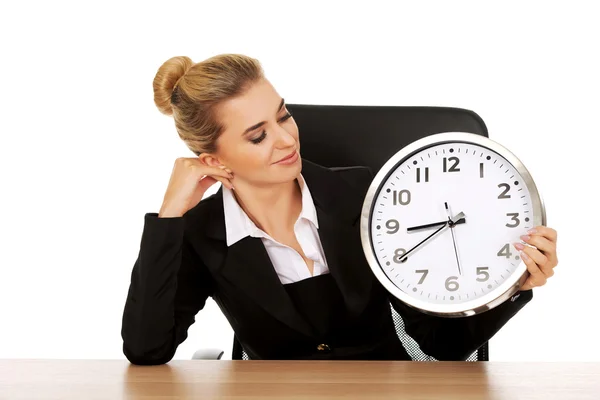 Zufriedene Geschäftsfrau mit Uhr hinter dem Schreibtisch lizenzfreie Stockbilder