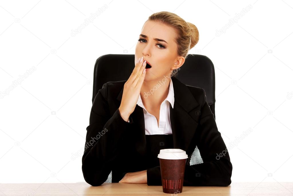 Yawning businesswoman drinking coffee from paper cup behind the desk