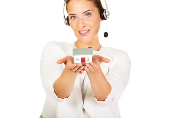 Młoda bizneswoman w słuchawkach posiada model domu — Zdjęcie stockowe