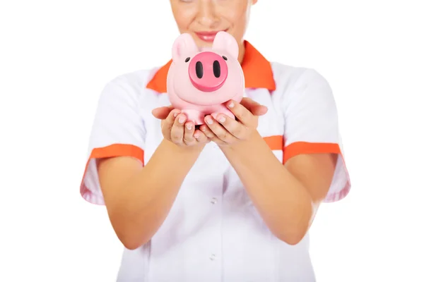 Junge schöne Ärztin oder Krankenschwester hält ein Sparschwein — Stockfoto