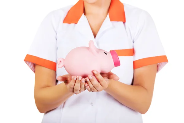Fiatal női orvos vagy a nővér egy piggybank gazdaság — Stock Fotó