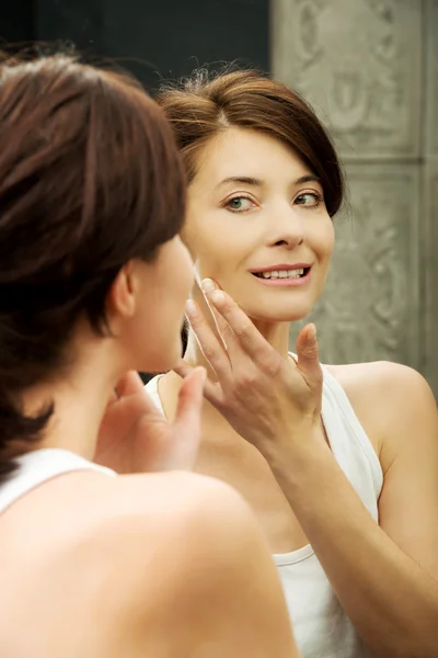 Mujer poniendo crema anti-envejecimiento en su cara . — Foto de Stock