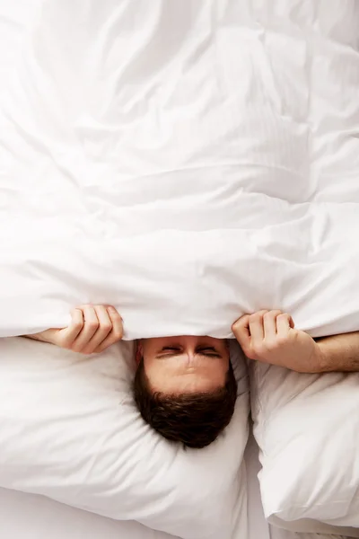 Hombre escondido en la cama bajo sábanas . — Foto de Stock