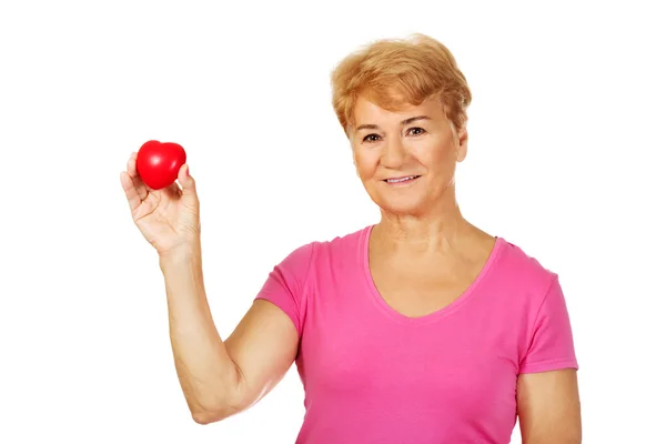 Old smiling woman holding red toy heart — Stock Photo, Image