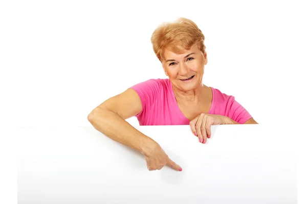 Oudere vrouw wijst naar iets op een leeg spandoek — Stockfoto