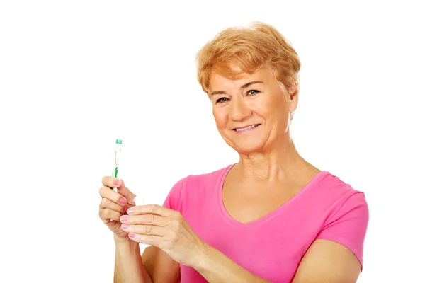 Sorrindo mulher idosa segurando pasta de dentes e escova de dentes — Fotografia de Stock