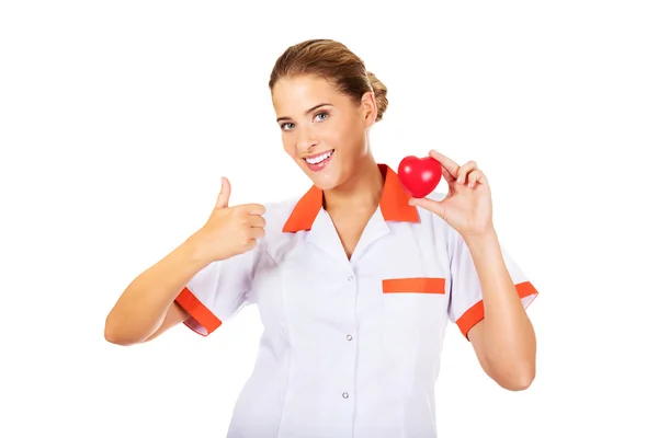 Γυναίκα γιατρό ή νοσοκόμα κρατώντας το παιχνίδι καρδιά και δείχνει τον αντίχειρα επάνω — Φωτογραφία Αρχείου