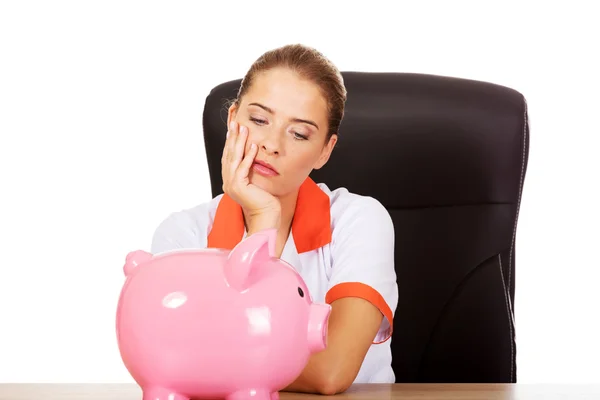 Sad female doctor with piggy bank — Stock Photo, Image