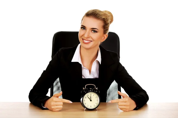 Happy businesswoman with alarm clock behind the desk — Stock Photo, Image