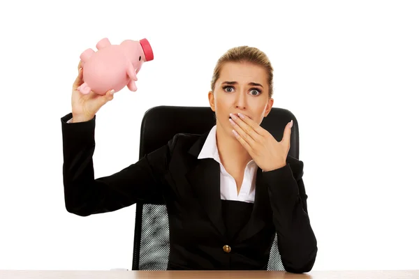 Worried businesswoman with a piggybank behind the desk — Stock Photo, Image