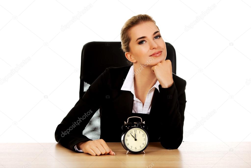 Happy businesswoman with alarm clock behind the desk