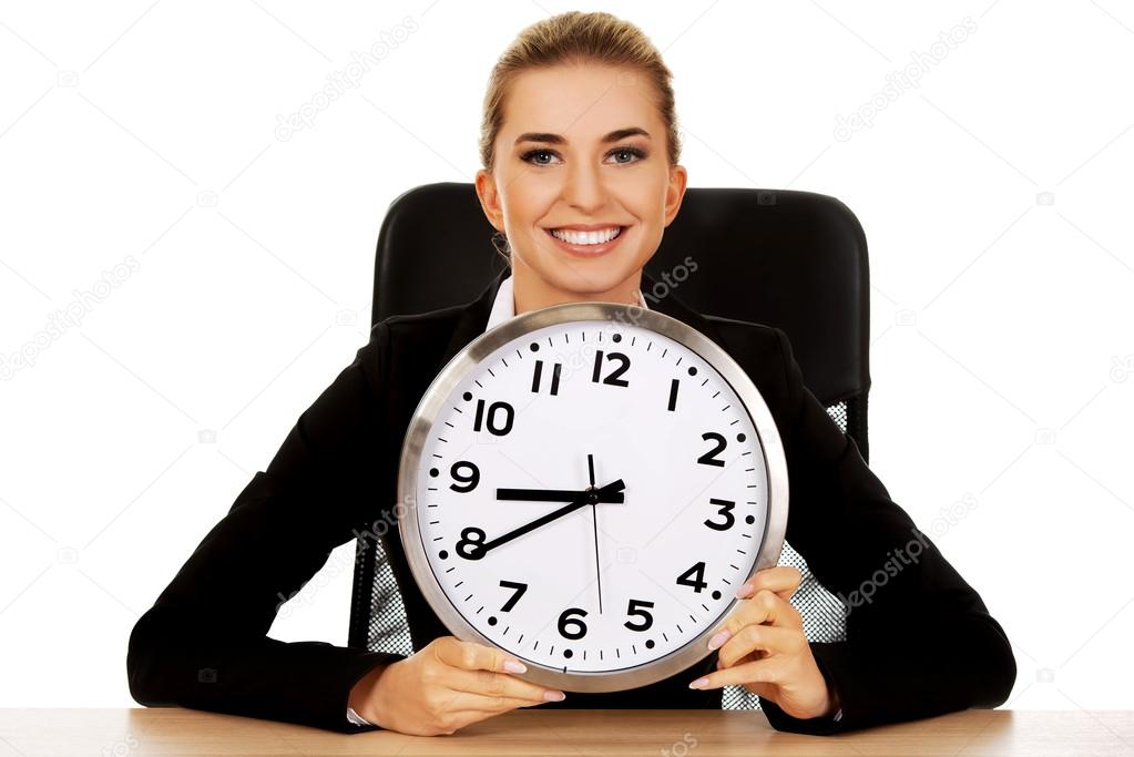 Happy businesswoman with clock behind the desk