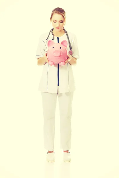 Ung kvinnlig läkare innehar en piggybank. — Stockfoto
