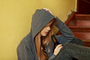 Genç bunalımlı kadın merdivenlerde oturuyor ve bira içiyor.