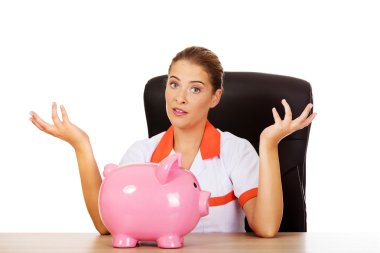 Female doctor  sitting behind the desk and holding a piggybank clipart