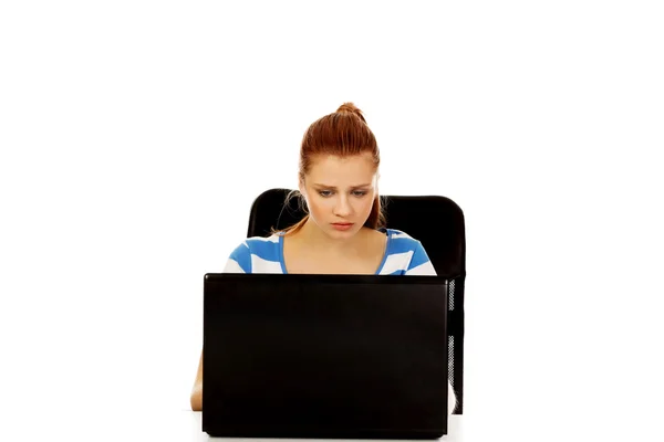 Teenage angry woman with laptop sitting behind the desk — Stock Photo, Image