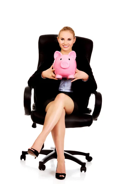 Mulher de negócios sentado em poltrona e segurando piggybank — Fotografia de Stock