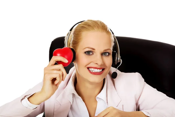 Happy call center kvinna sitter bakom skrivbordet och hålla hjärtat modell — Stockfoto