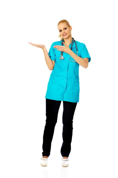 Smiling female doctor or nurse presenting copyspace or something on open palm and pointing for this — Stock Photo, Image