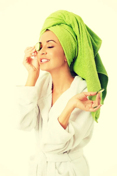 Woman in bathrobe applying cucumber on eyes — Stock Photo, Image