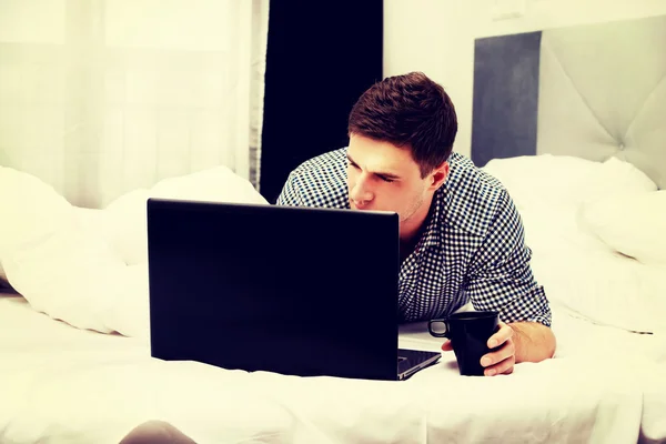 Przypadkowy młody człowiek za pomocą laptopa w łóżku w domu. — Zdjęcie stockowe