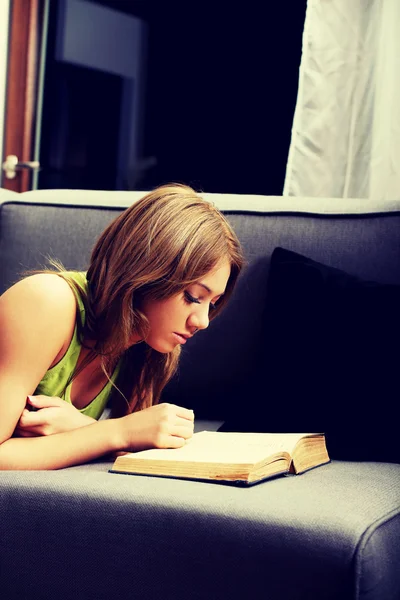 Mujer joven leyendo un libro en el sofá . — Foto de Stock