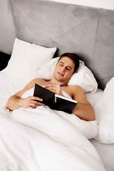 Hombre escribiendo una nota en su cama . — Foto de Stock